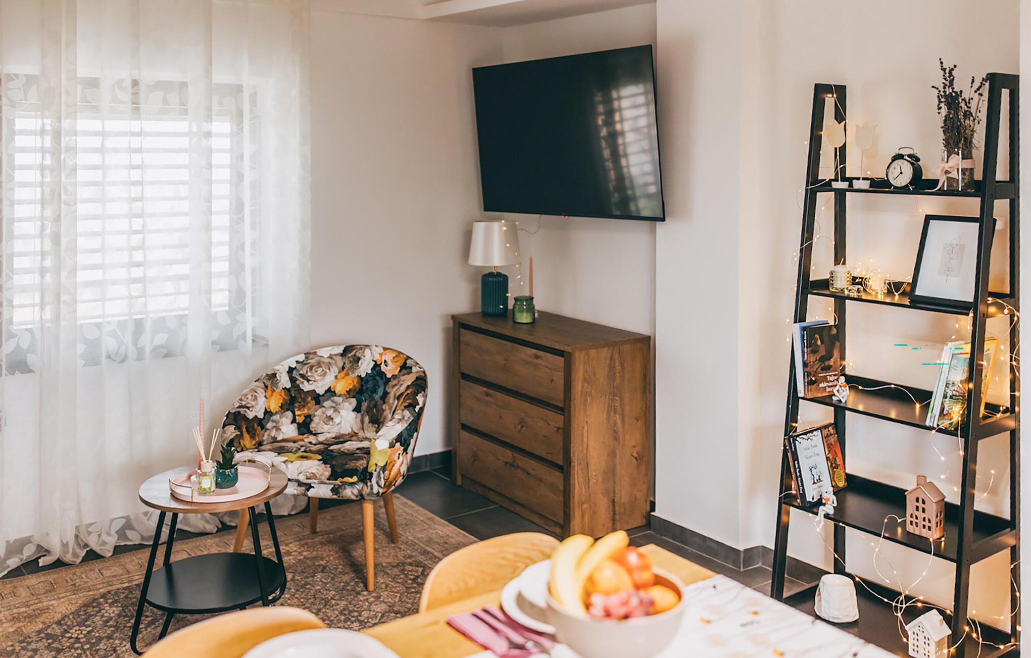 Een woonkamer met een bank, een houten kast, een televisie, een boekenkast en een eethoek met een tafel en stoelen.