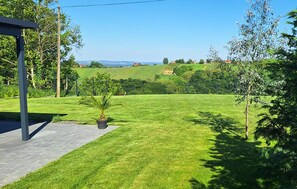 A well-maintained lawn with a small palm tree, a paved walkway, and a clear view of distant hills. - Cozy home in Banfi with sauna (Banfi)