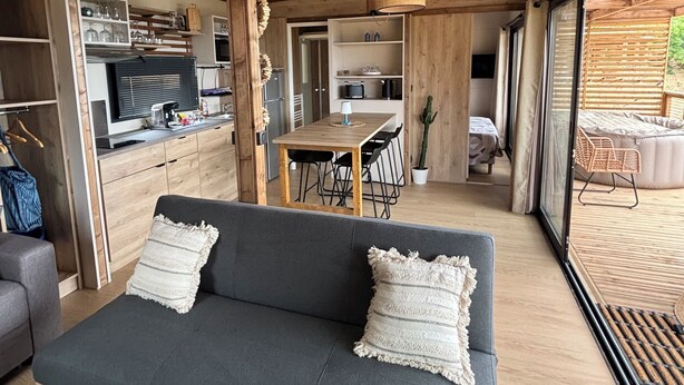 Un intérieur chaleureux avec un canapé, une table à manger, un coin cuisine et de grandes fenêtres.