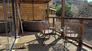 Un espace extérieur abrité, doté d’un plancher en bois, de chaises en osier et offrant une vue sur un paysage montagneux.
