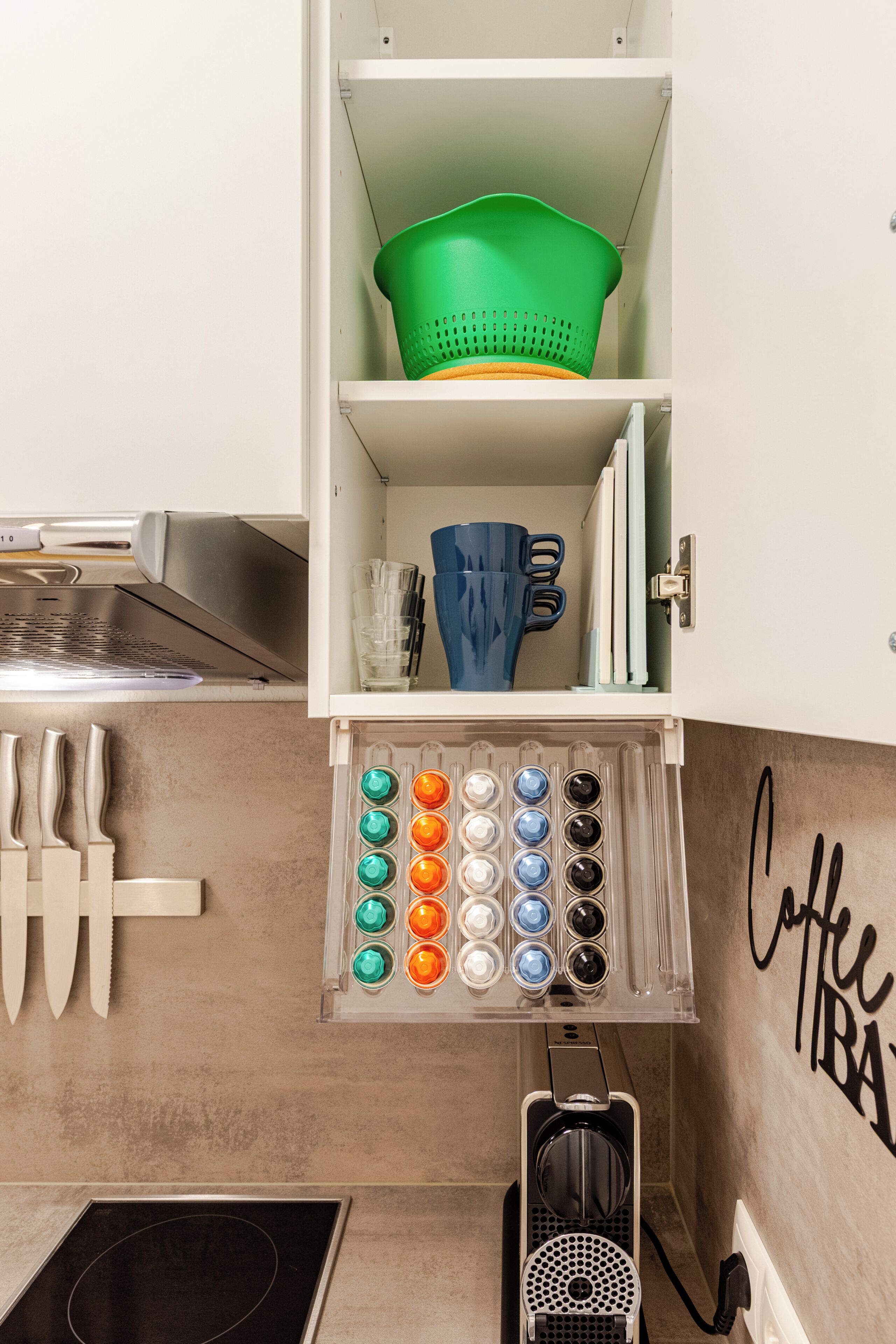 A kitchen with a coffee machine, a sink, and a cabinet with various utensils and containers.