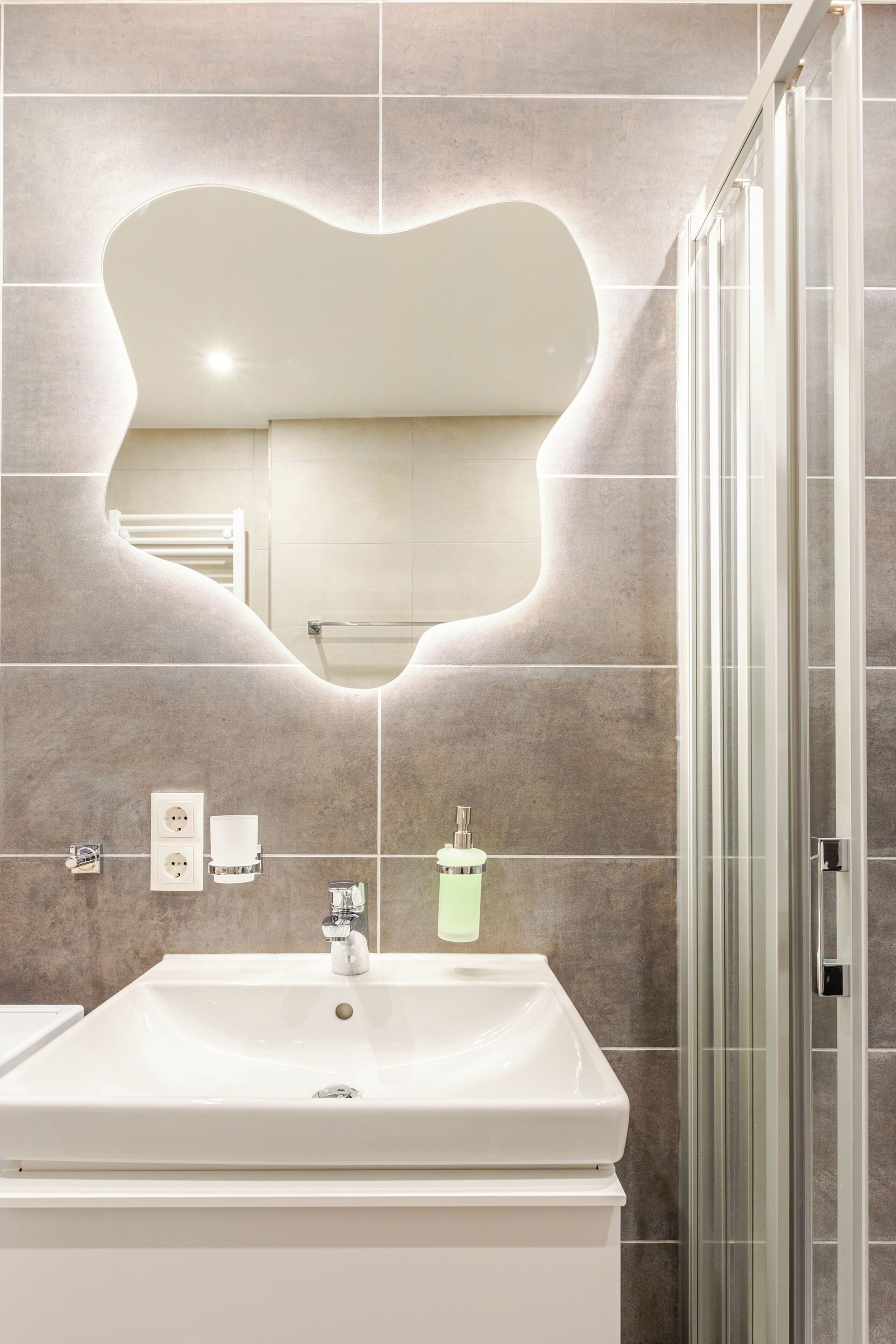 Ein Badezimmer mit spiegelartigem Spiegel, einem weißen Waschbecken und einer Duschkabine aus Glas.