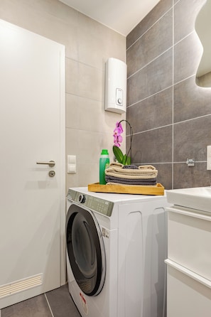 A modern bathroom with a white washing machine, a green bottle, and a pink orchid on top. - ★Koblenz City Studio I Near main station & center vacation apartment★ (Koblenz)