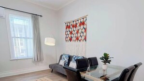 Un saló modern amb un sofà, una taula de centre de vidre, una làmpada i un penjall decoratiu a la paret.