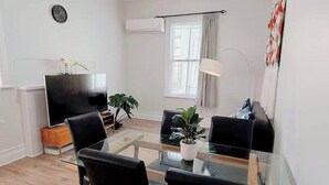 Un saló modern amb taula de dinar de vidre, cadires negres, televisió plana, una planta en test i una finestra amb cortines.