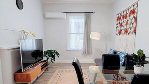 Un saló modern amb televisió de pantalla plana, taula de dinar amb cadires, sofà, taula de centre i una finestra gran amb cortines.