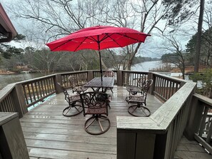A wooden deck with a table and chairs, a red umbrella, and a view of a body of water. - Spacious Lakefront Apt w/ Deck in Fayetteville! (Fayetteville)
