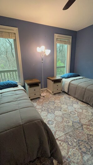 Quarto com duas camas, uma luminária de chão e janela com vista para árvores.