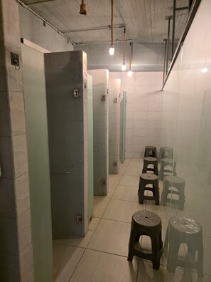 A public restroom with multiple stalls, a glass partition, and plastic stools. - Hotel Capsula Condesa (Mexico City)