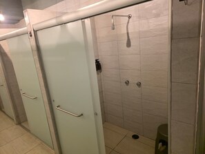 A row of restroom stalls with a shower area, each stall has a door with a handle, and the floor is tiled.