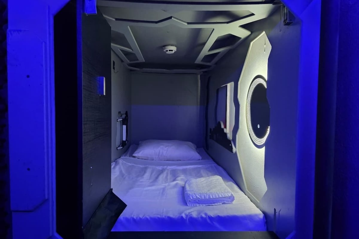 Une pièce de taille modeste, avec un lit simple, une petite fenêtre et un luminaire rond.