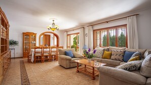 A living room with a dining table, two sofas, a chandelier, and a view of greenery outside. - Chic 12-guest Villa With Pool in Ibiza (Santa Eulalia del Rio)