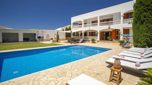A swimming pool with lounge chairs, a stone patio, and a white building with balconies. - Chic 12-guest Villa With Pool in Ibiza (Santa Eulalia del Rio)