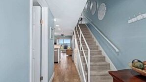 Un couloir avec un escalier, une porte et une vue sur un espace cuisine.