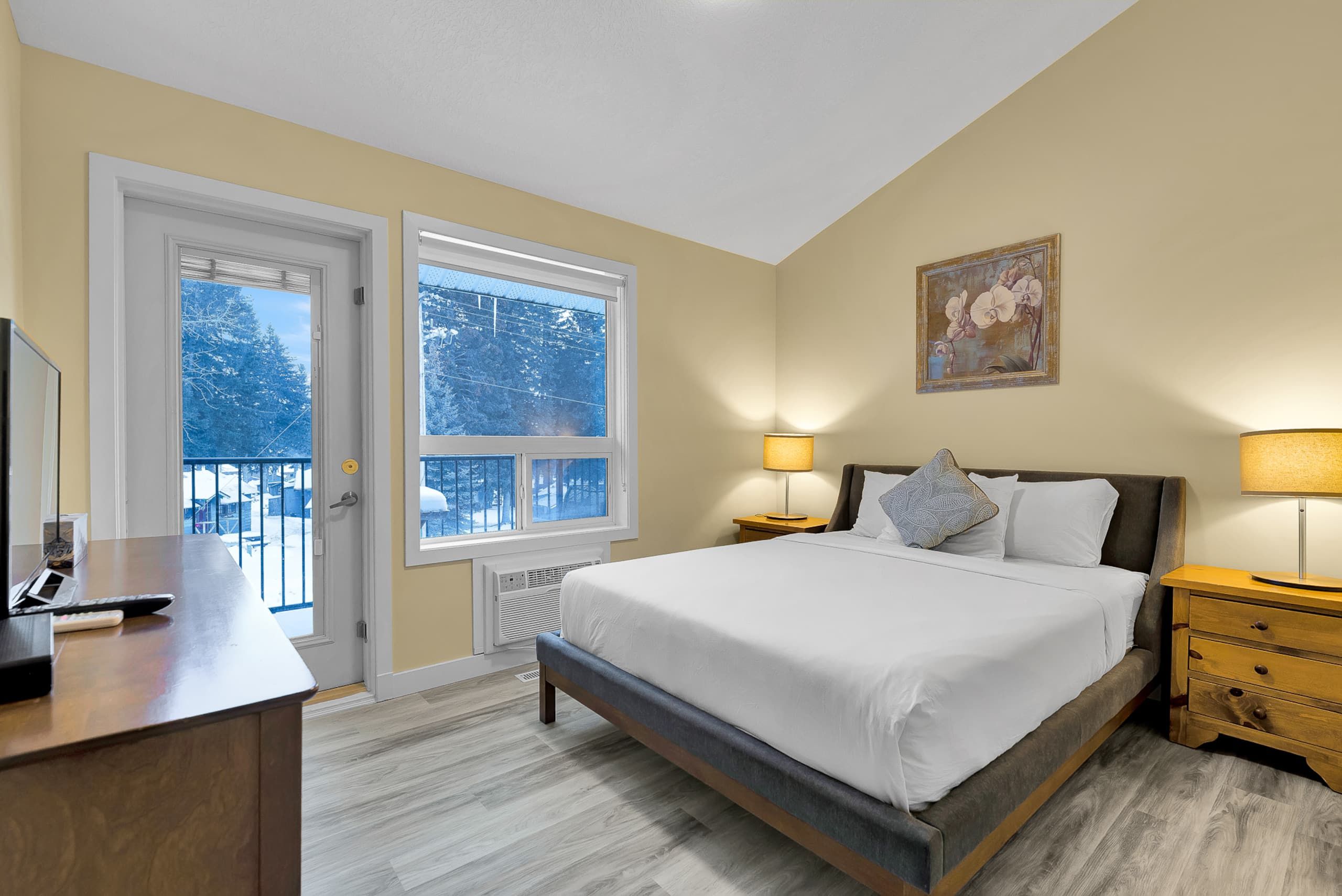 Une chambre d’hôtel avec un lit, des tables de chevet, un bureau et une fenêtre donnant sur des arbres couverts de neige.