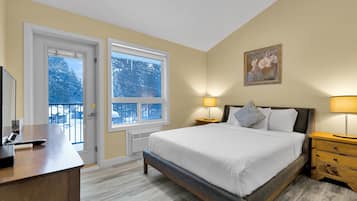 Une chambre d’hôtel avec un lit, des tables de chevet, un bureau et une fenêtre donnant sur des arbres couverts de neige.
