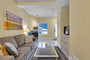 A living room with a sofa, a glass coffee table, a fireplace, and a television. - B246- Townhouse near Banff gate, Free Parking (Harvie Heights)