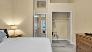 Habitación de hotel con cama, mesita de noche, lámpara, cómoda de madera y vestidor con ropa colgada.