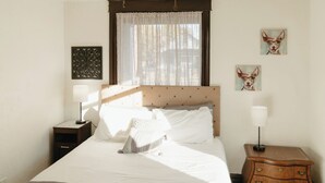 Un dormitorio con cama, mesita de noche, ventilador de techo, ventana con cortinas y decoración en la pared.