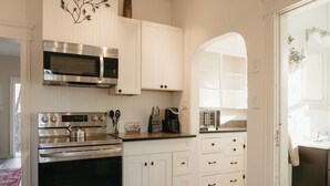 Una cocina con armarios blancos, microondas, horno y cafetera.