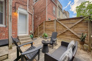Eine Terrasse mit Gartenmöbeln, einem Holzzaun und einem Backsteinhaus.