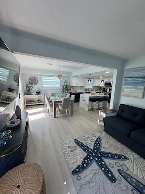A modern living room with a starfish rug, a dark sofa, and a dining area with a table and chairs. - Fantastic 3-bedroom house with walking distance to the serene Madeira Beach. (Madeira Beach)