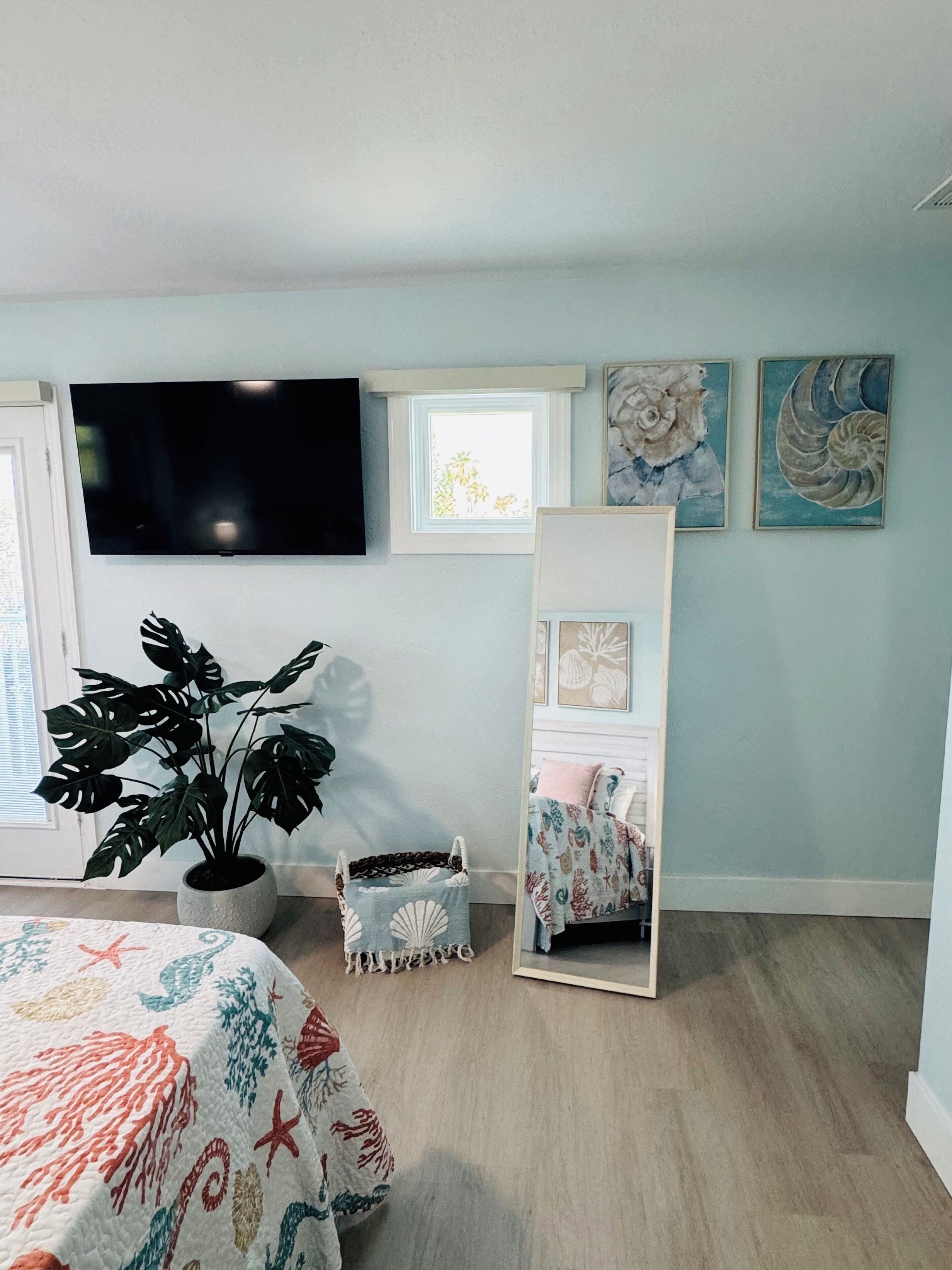 Een slaapkamer met een bed, een kamerplant, een televisie, een raam en kunst aan de muur.