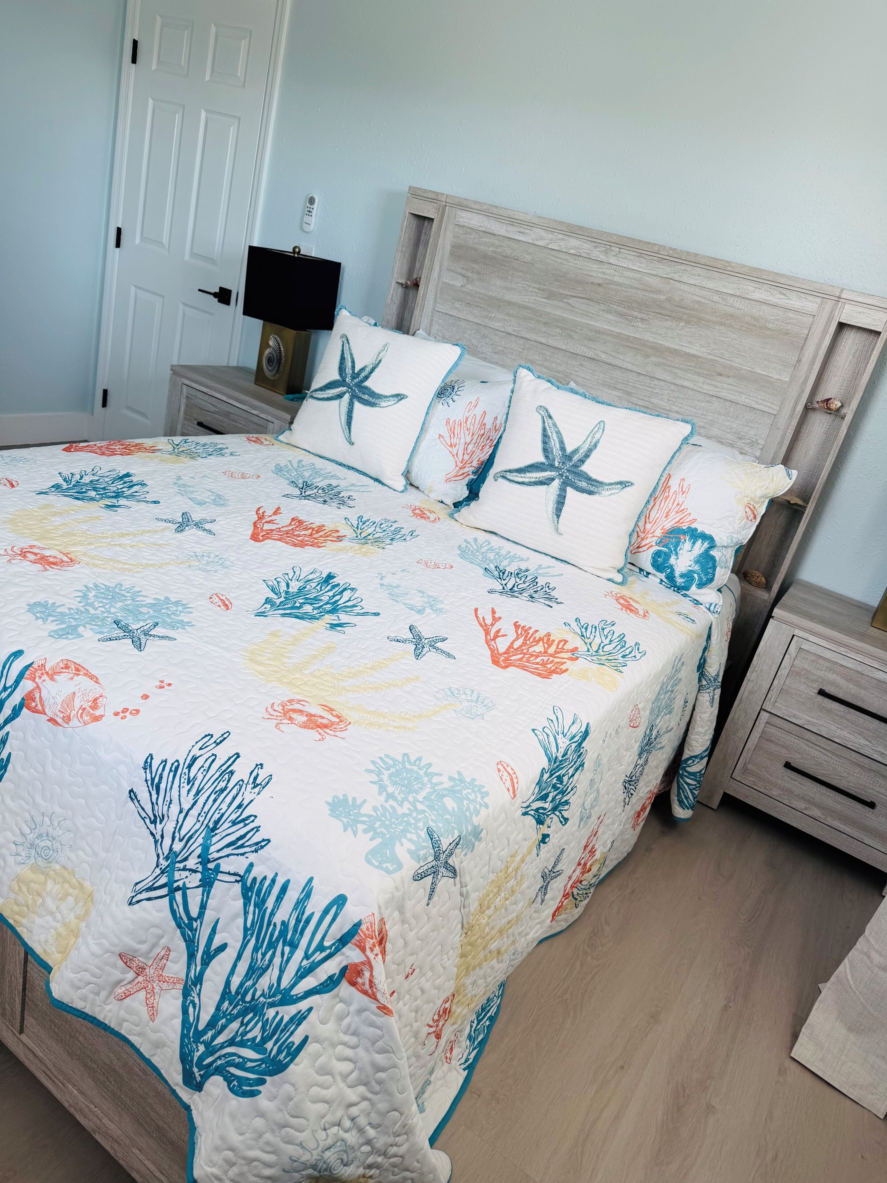 Ein Bett mit einem floralen und sternförmigen Muster, ein Holzkopfende, ein Nachttisch mit einer Lampe und eine weiße Tür.
