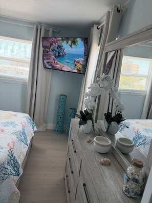 Ein Schlafzimmer mit Bett, Schminktisch, Fernseher und einem Fenster mit Vorhängen.