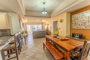 A dining area with a wooden table, benches, and a kitchen in the background. - Bonita 405, Las Palmas Resort (Puerto Peñasco)