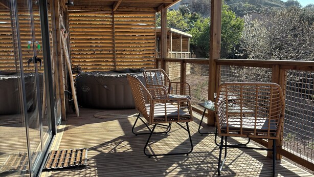 Un espacio exterior cubierto con suelo de madera, sillas de mimbre y vistas a un paisaje montañoso.