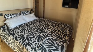 Una cama con colcha estampada, un televisor montado en la pared y vigas de madera en el techo.