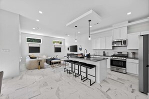Una cocina moderna con armarios blancos, una isla central con taburetes de bar, horno empotrado y microondas.