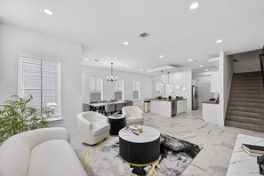 A spacious living area with a dining table, seating, a kitchen, and a staircase. - Upscale Home, Office, Galleria & NRG (Houston)