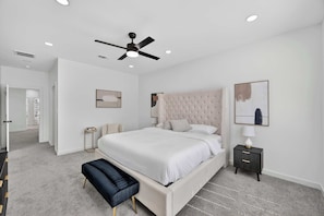 A bedroom with a large bed, a ceiling fan, recessed lighting, a bedside table with a lamp, and artwork on the walls. - Sophisticated Home, Office, Galleria & NRG (Houston)