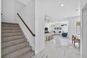 Un intérieur moderne avec un escalier recouvert de moquette, un coin repas doté de tabourets de bar et un espace salon avec un canapé bleu.