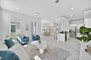 A modern living room with a sofa, a coffee table, and a kitchen area in the background. - Sophisticated Home, Office, Galleria & NRG (Houston)