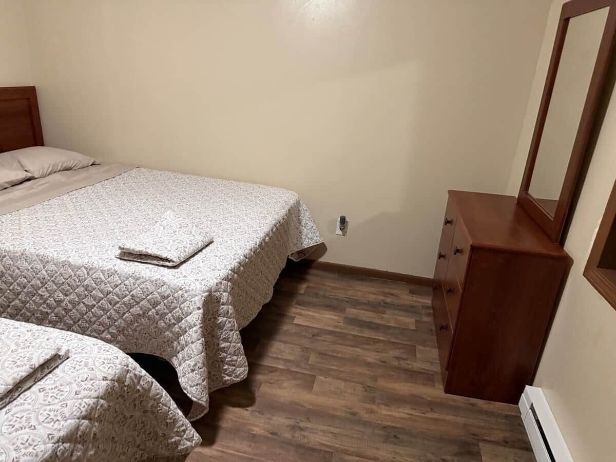A bedroom with two beds, a wooden dresser, and a mirror.