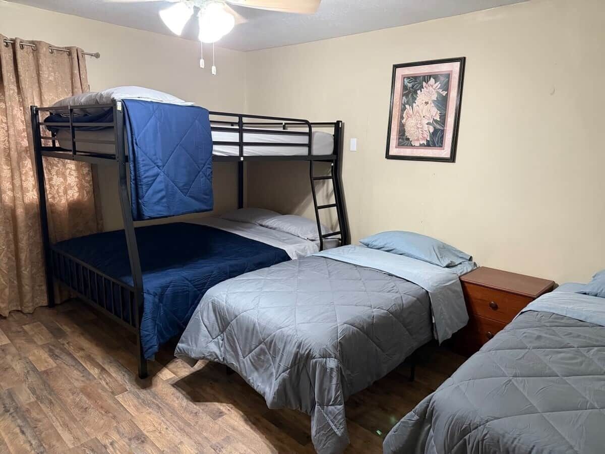 Une chambre avec un lit superposé, un ventilateur de plafond, un plancher en bois et un tableau floral encadré accroché au mur.