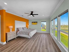 Une chambre à coucher avec un lit, des tables de chevet, un ventilateur de plafond et de grandes fenêtres.