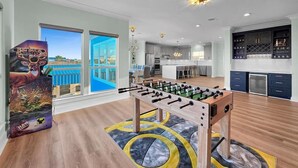 A spacious living area with a foosball table, a kitchen, and a large window with a view. - Serene 4-bedroom house with AC in Bolivar Peninsula (Bolivar Peninsula)