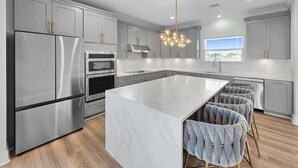 A modern kitchen with stainless steel appliances, a marble island, and bar stools. - Serene 4-bedroom house with AC in Bolivar Peninsula (Bolivar Peninsula)