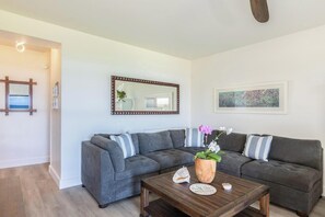 A modern living room with a sectional sofa, a wooden coffee table, a mirror, and a framed picture on the wall. - ALL NEW Oceanfront 2 storey comfortably sleeps 6-7 (Lihue)