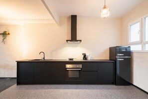 A modern kitchen with a black countertop, stainless steel appliances, and a hanging light fixture. - Grand Central 2BR Apartment (Antwerp)