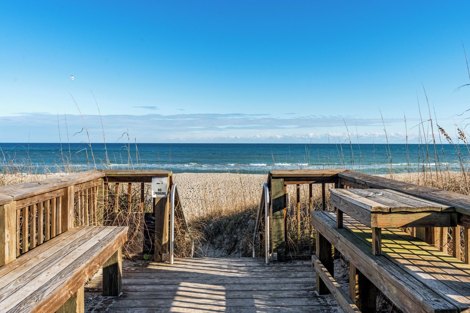Ein hölzerner Gehweg führt zu einem Strand, mit einem 'Nicht Rauchen'-Schild.
