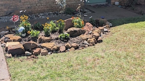 A landscaped garden with a variety of plants and decorative elements, including rocks and a bird bath.