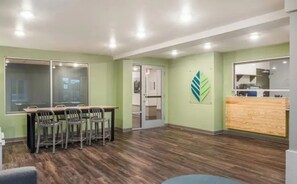 A conference room with a wooden table and chairs, a reception desk, and a green wall with a leaf design. - Stay Together, Group-Friendly Compound Near Austin Highlights – 4 Queen Units (Austin)