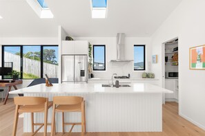 A modern kitchen with a central island, stainless steel appliances, and a view of the outdoors. - New Bach 10 minutes walk from Langs Beach with 3 bdrm + 2 Bathrooms (Waipu)