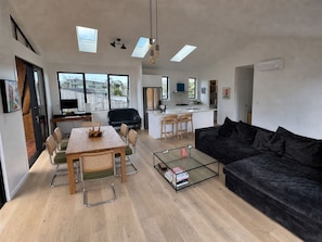 A modern living space with a dining area, a black sofa, a glass coffee table, and a kitchen area.