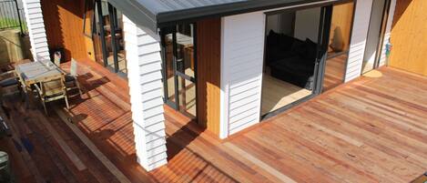 A modern house with a wooden deck, a patio with a table and chairs, and a sliding glass door leading to an interior space.